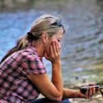 Frau mit Handy sitzt traurig am See