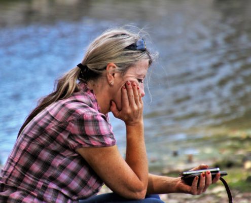 Frau mit Handy sitzt traurig am See